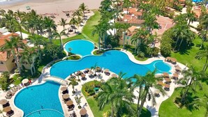 Vista aèria d'un complex turístic amb diverses piscines, palmeres i accés a la platja.