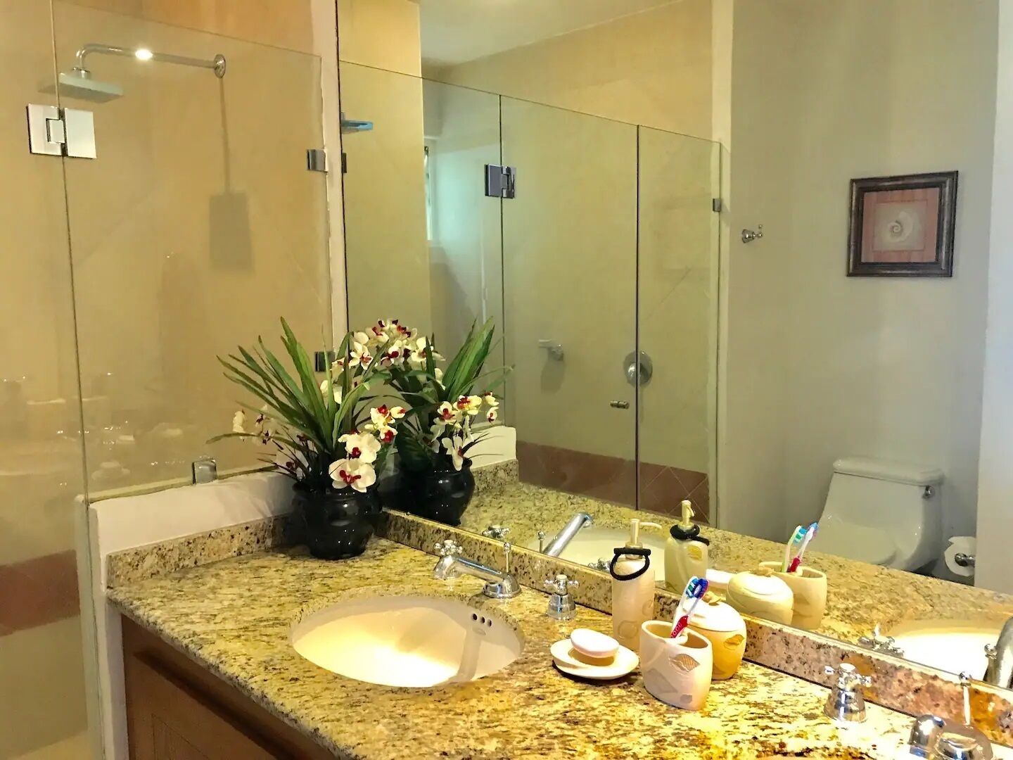 A bathroom with a granite countertop, two sinks, a large mirror, and a glass shower enclosure.