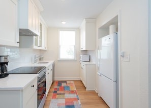 A compact kitchen with white cabinets, a stainless steel range, a microwave, and a refrigerator.