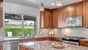 A modern kitchen with wooden cabinets, a stainless steel dishwasher, a granite countertop, a built-in oven, and a large window overlooking a garden. - Casa Bonita with Private Pool / 4B/2B sleeps 8 in Old Town Scottsdale (Scottsdale)