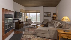 A cozy living room with a fireplace, comfortable seating, and large windows offering a view of the outdoors. - Eolus 321 - Managed by Purgatory Result (Durango)