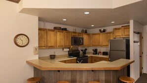A compact kitchen with wooden cabinets, a central island with stools, a microwave, a stove, and a refrigerator. - Eolus 321 - Managed by Purgatory Result (Durango)