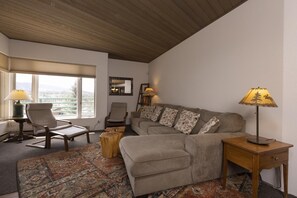 Relax in this inviting living room with a high ceiling, comfortable sofa, and large window offering a view of the outdoors.