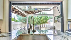 Une cuisine dotée d’un grand évier, d’un robinet et donnant sur une cour arrière avec des arbres et une maison.