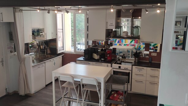 A compact kitchen with white cabinets, a central island with chairs, and a window providing natural light. - 25-person apartment 10 minutes from Avignon, Bagnols sur Cèze, Marcoule, (Roquemaure)