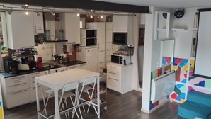 A modern kitchen with white cabinets, a dining area with a white table and chairs, and a colorful abstract wall design. - 25-person apartment 10 minutes from Avignon, Bagnols sur Cèze, Marcoule, (Roquemaure)