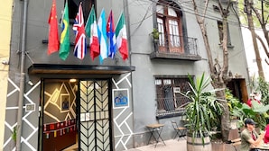Edifici amb diverses banderes, un cartell de 'Roomies' i una entrada tancada per una porta.