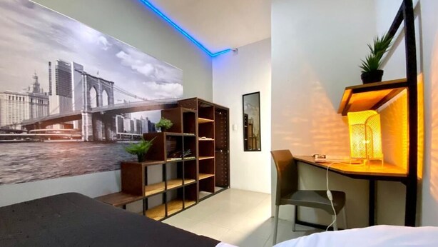 Habitació d'hotel moderna amb un llit, un escriptori amb una cadira, una prestatgeria i una estant mural amb una planta.