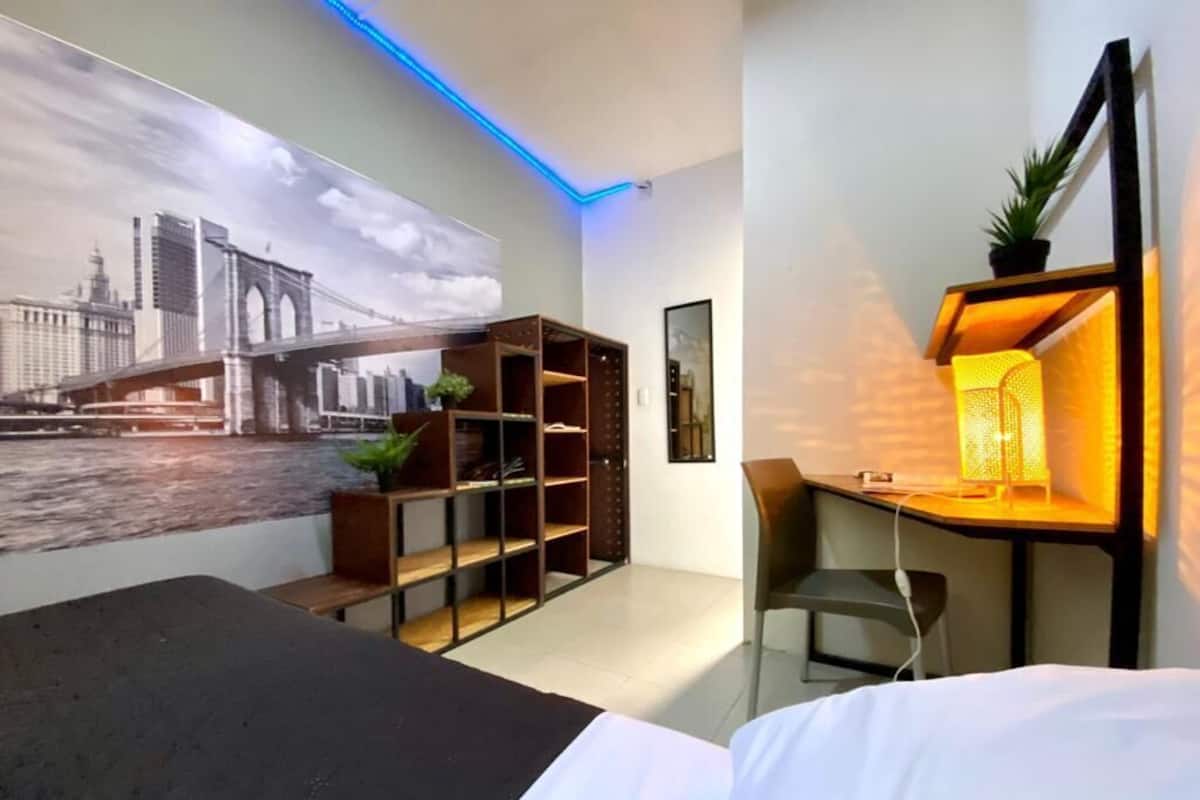 Una habitación de hotel moderna con una cama, un escritorio con una silla, una estantería y un estante con una planta.