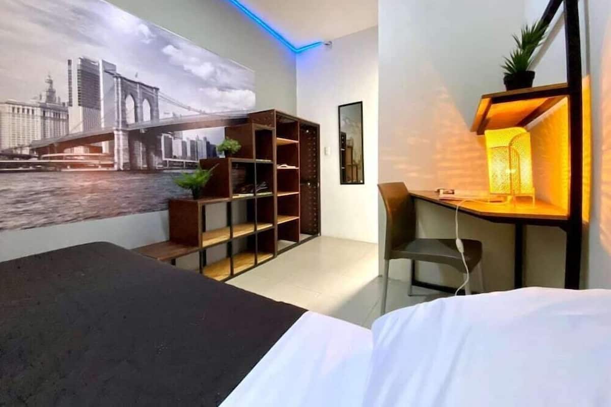 Una habitación de hotel moderna con una cama, un escritorio con una lámpara, una estantería y un mural en la pared de un puente.