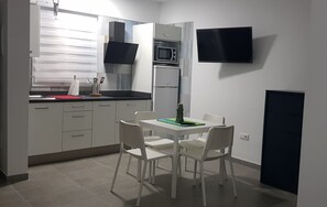 A compact kitchen with a dining area, a microwave, a stove, and a flat-screen TV mounted on the wall.