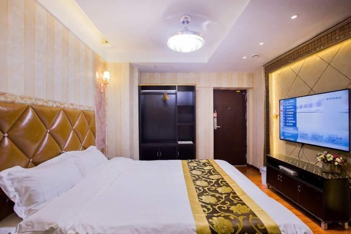 A hotel room with a large bed, a television, a wardrobe, and a ceiling light.