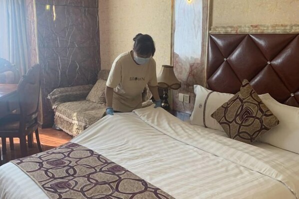 A hotel room with a large bed, a smaller sofa, a wooden chair, and a lamp.