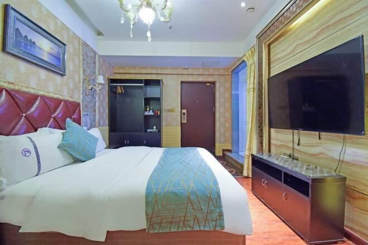 A hotel room with a bed, a TV, a minibar, and a door leading to a bathroom.