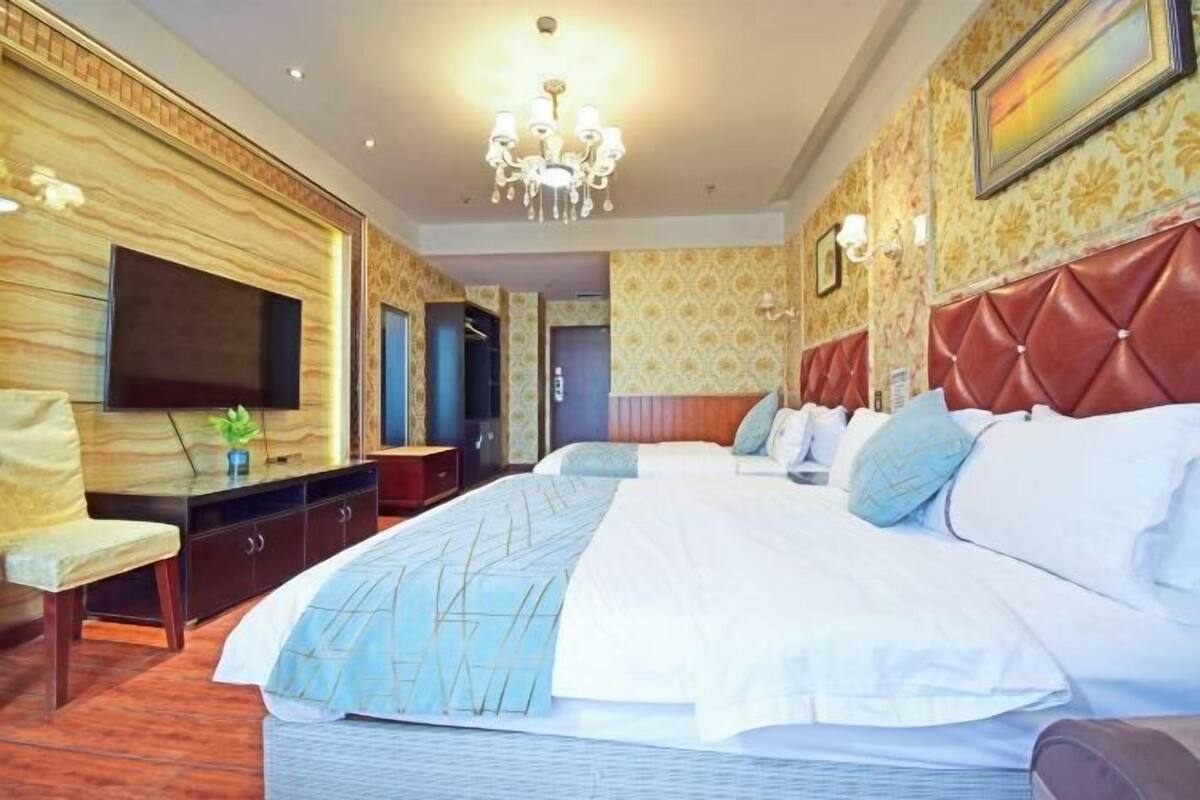 A hotel room with a large bed, a television, a chandelier, and a red headboard.