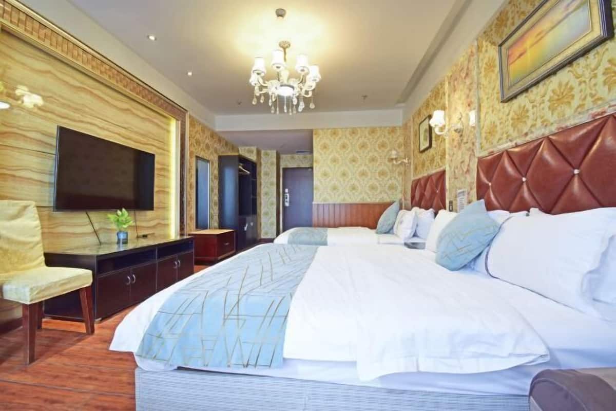 A hotel room with a large bed, a television, a desk with a chair, and a chandelier.