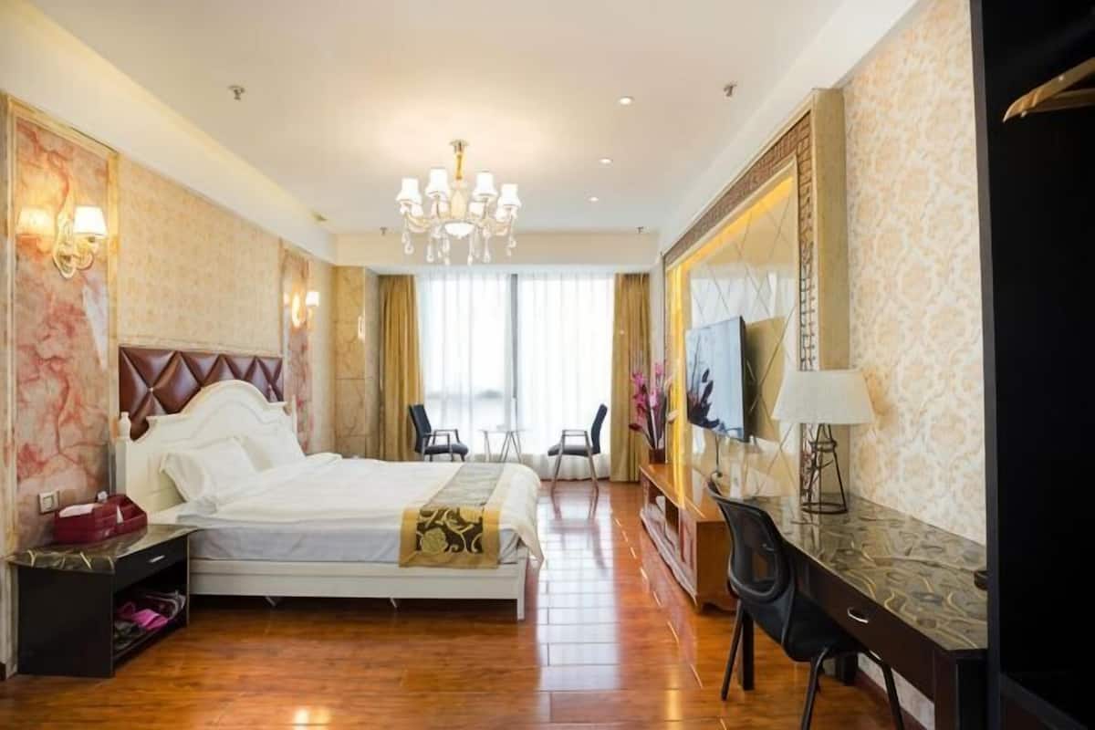 A hotel room with a large bed, a desk with a chair, a TV, and a chandelier.