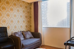 A room with a patterned wallpaper, a sofa with cushions, a chair, and a view of buildings through a window. - Yidun Hotel (Chongqing)