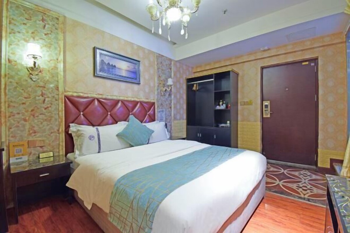 A hotel room with a large bed, a wardrobe, a nightstand, and a chandelier.
