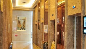 Un pasillo de hotel con paredes de mármol, una obra de arte enmarcada y una pantalla digital en la pared.