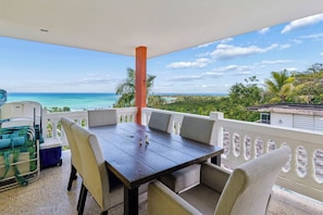 A balcony with a table and chairs, overlooking a beach and ocean.