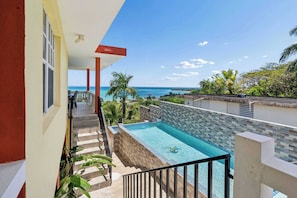 Uma piscina com vista para o oceano, uma escadaria e uma varanda.
