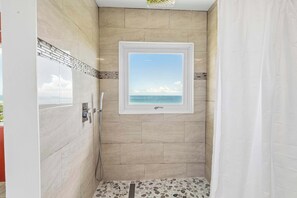 A shower with a view of the sea, a window, and a tiled floor.