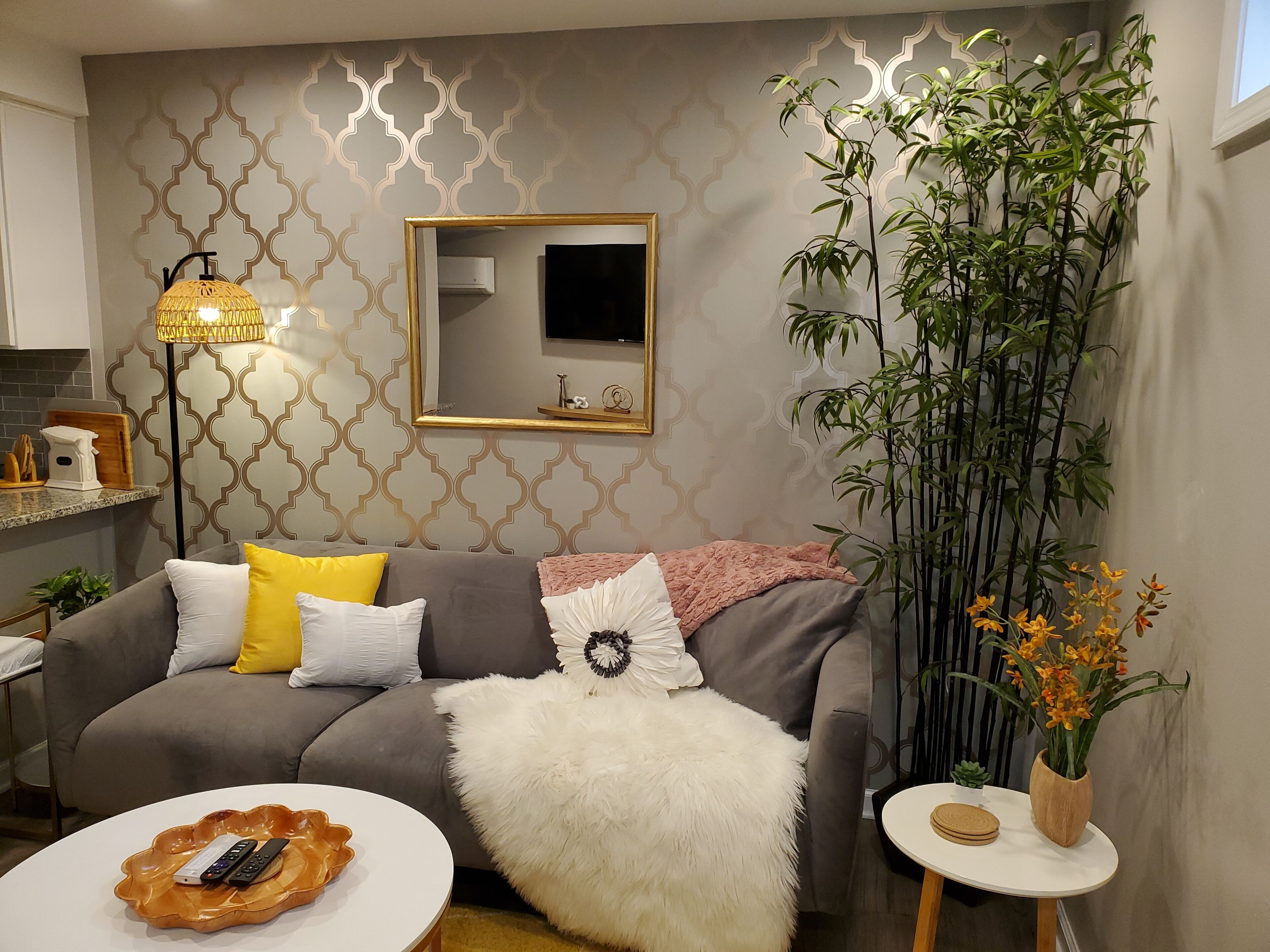 Een moderne woonkamer met een grijze bank, een zachte witte plaid en een klein wit tafeltje met een afstandsbediening.