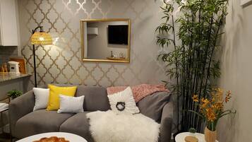 Een moderne woonkamer met een grijze bank, een zachte witte plaid en een klein wit tafeltje met een afstandsbediening.
