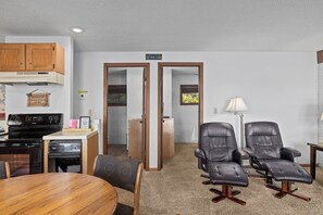 A compact living space with a kitchenette, a dining area, and two leather chairs.