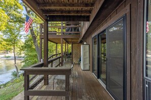 A wooden deck with a table and chairs, overlooking a body of water with trees and an American flag.