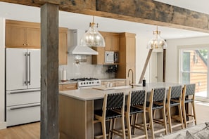 Eine moderne Küche mit Holzschränken, einem weißen Kühlschrank, einem Gasherd und einem Essbereich mit Tisch und Stühlen.