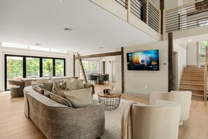 Ein geräumiges Wohnzimmer mit einem großen Ecksofa, einem Flachbildfernseher an der Wand und einer Treppe, die in einen oberen Bereich führt.