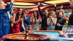 A group of people celebrating at a casino with a roulette table and slot machines.