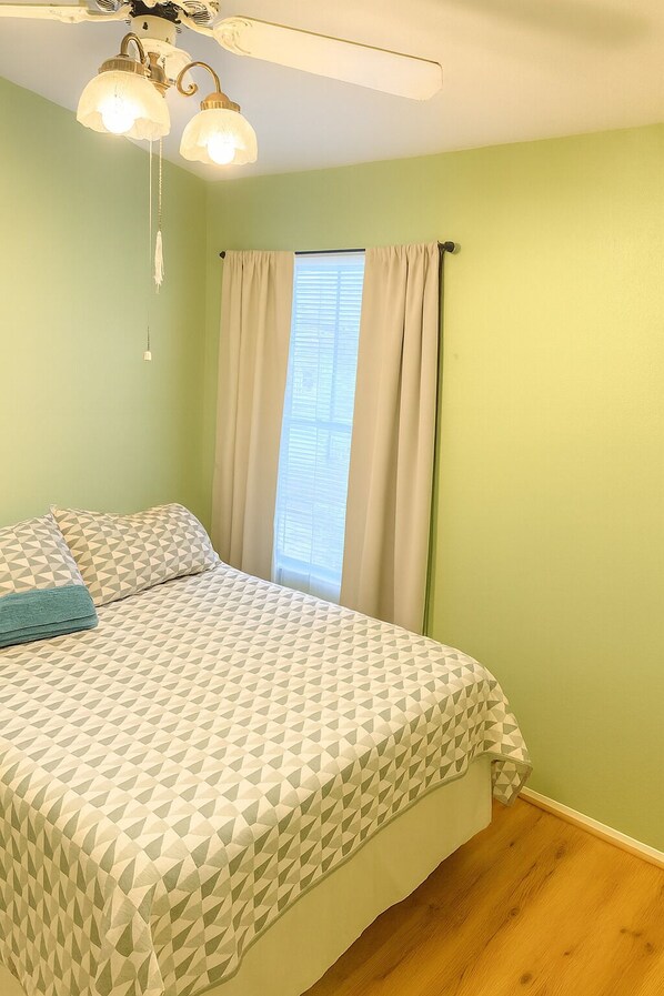 Un dormitorio con cama, ventilador de techo y ventana con cortinas.