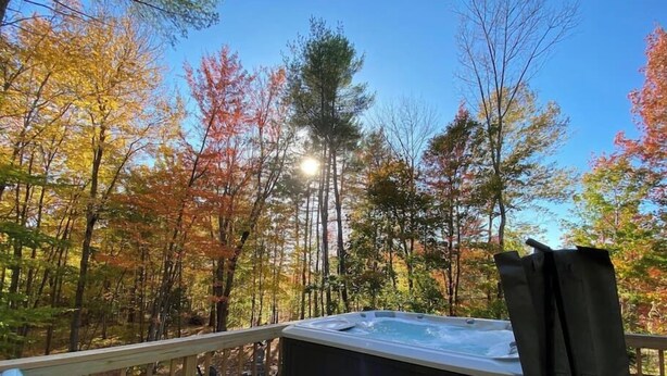 Una vasca idromassaggio su un pontile di legno con vista sugli alberi autunnali.