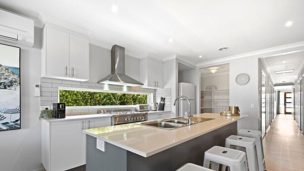 A modern kitchen with white cabinetry, a central island with stools, a built-in herb garden, and a stainless steel range hood.