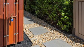 A wooden outdoor shower enclosure with a showerhead, a towel rack, and a metal handle.