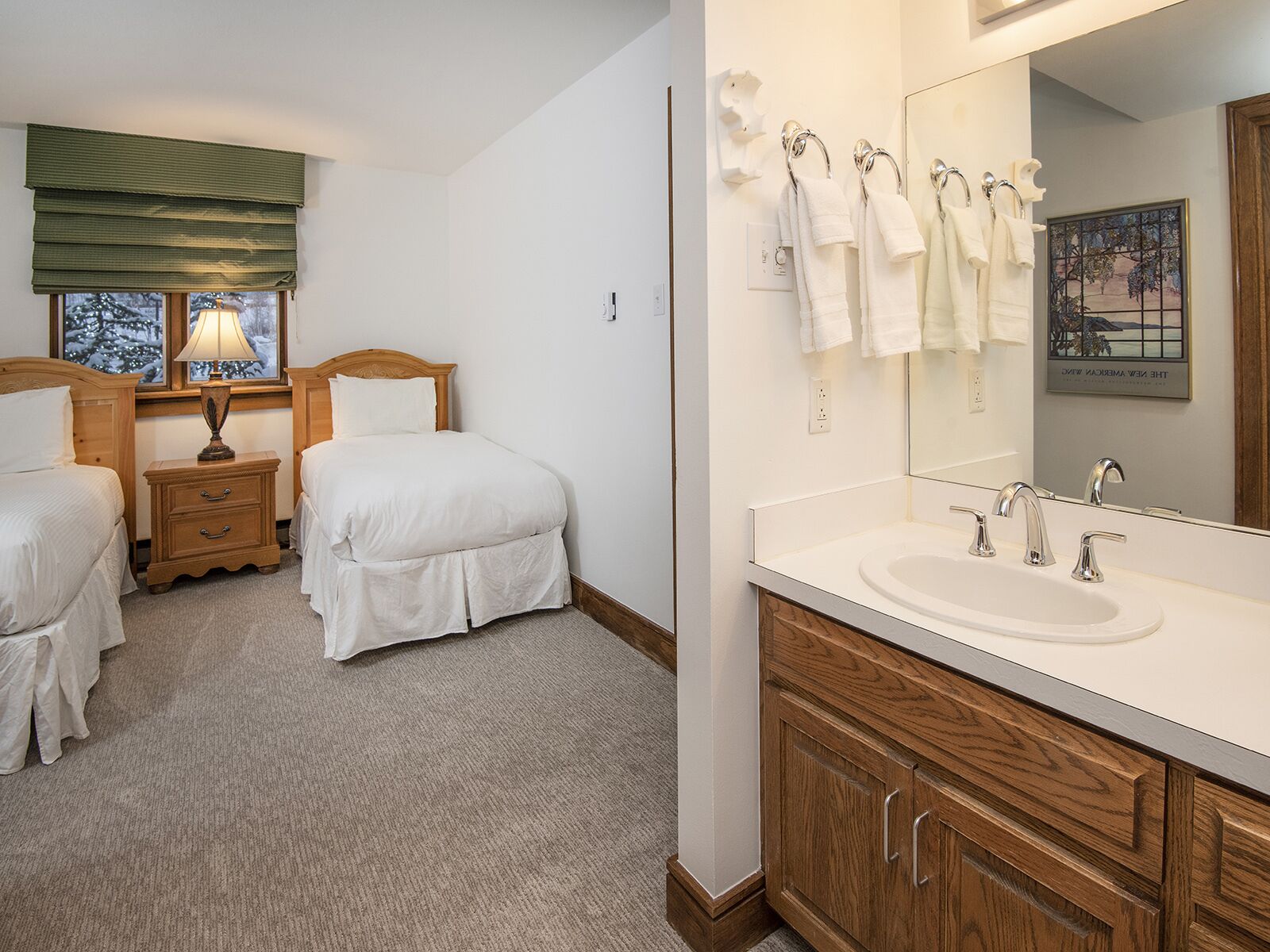 Une chambre d’hôtel avec deux lits, un grand miroir, un lavabo et une fenêtre donnant sur des arbres.