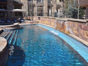 A rectangular pool with clear blue water, surrounded by stone walls and a stone building.