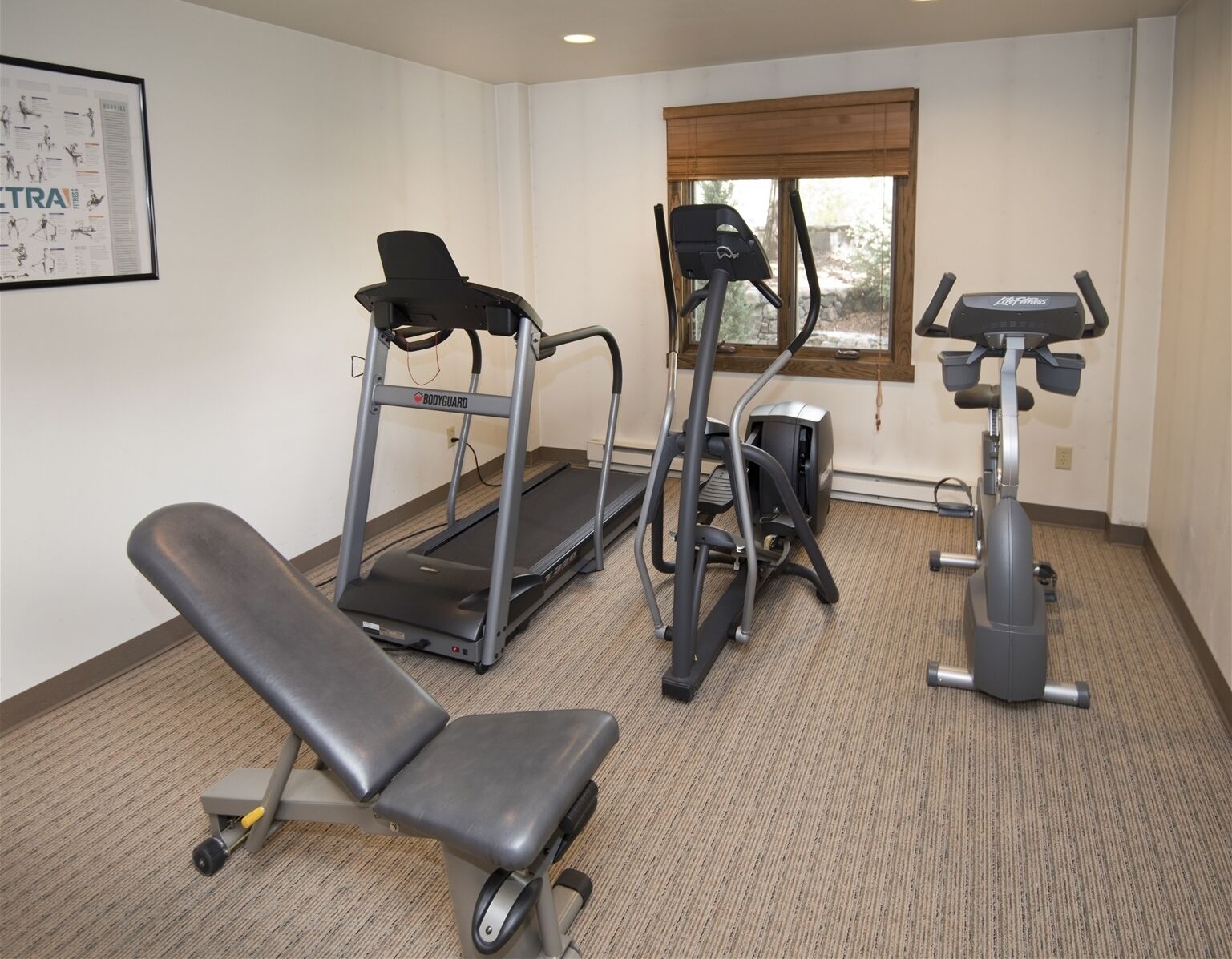 Une salle de sport équipée d’un tapis de course, d’un vélo elliptique et d’un banc de musculation.