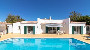 En hvid bygning med swimmingpool, grønne skodder og udendørs møbler.