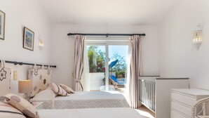 Et soveværelse med to senge, en kommode og en balkon med udsigt over have og pool.