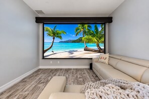 A room with a large window displaying a beach scene, a beige sofa, and a wooden floor.