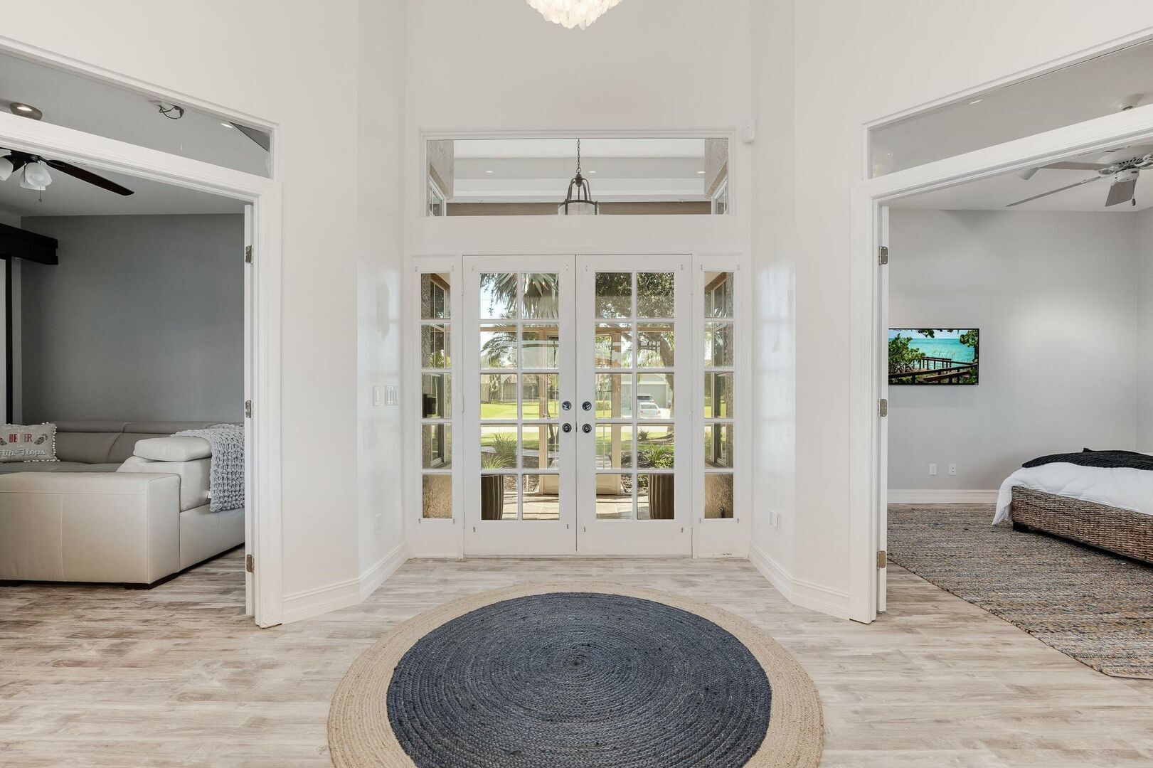 A spacious room with a large sliding glass door leading to a balcony, a comfortable sofa, a bed with a woven headboard, and a television on the wall.