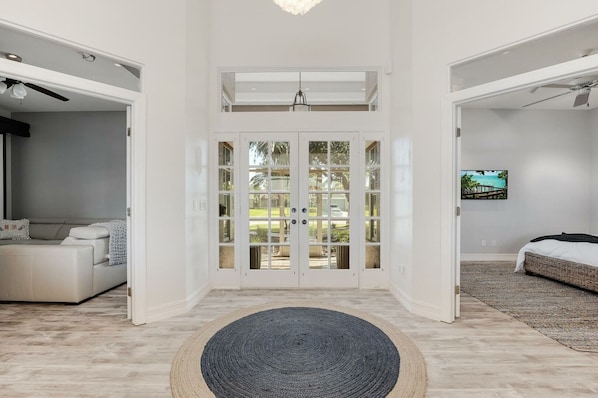 A spacious room with a large sliding glass door leading to a balcony, a comfortable sofa, a bed with a woven headboard, and a television on the wall.