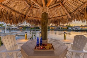 A thatched-roof outdoor seating area with a view of a marina and waterfront properties.