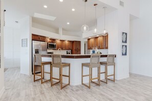 A modern kitchen with wooden cabinets, a central island with bar stools, and pendant lighting.