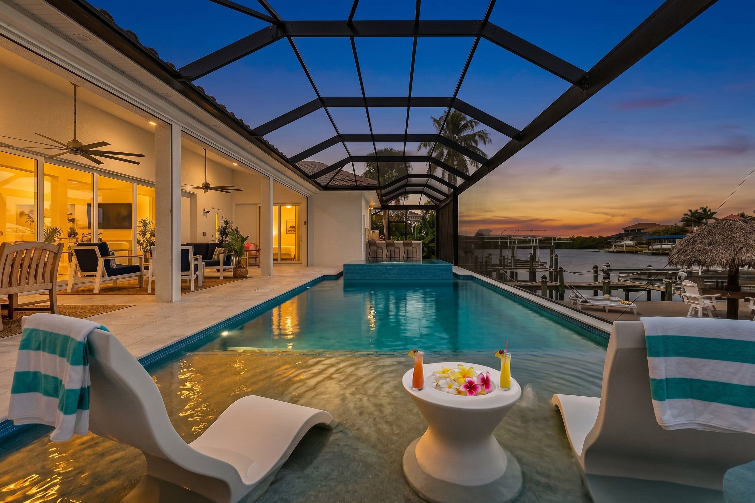 A swimming pool with a glass ceiling, lounge chairs, and a table with drinks.