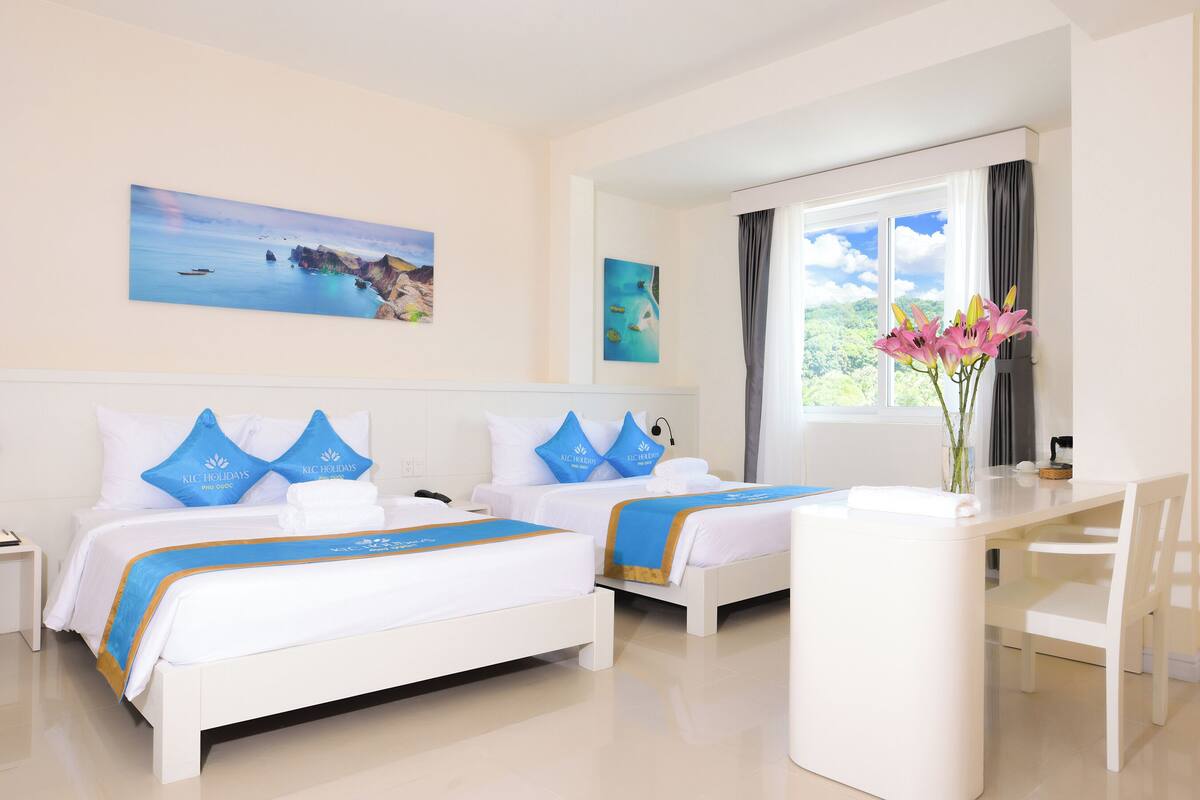 A hotel room with two beds, a desk, and a view of the sea.